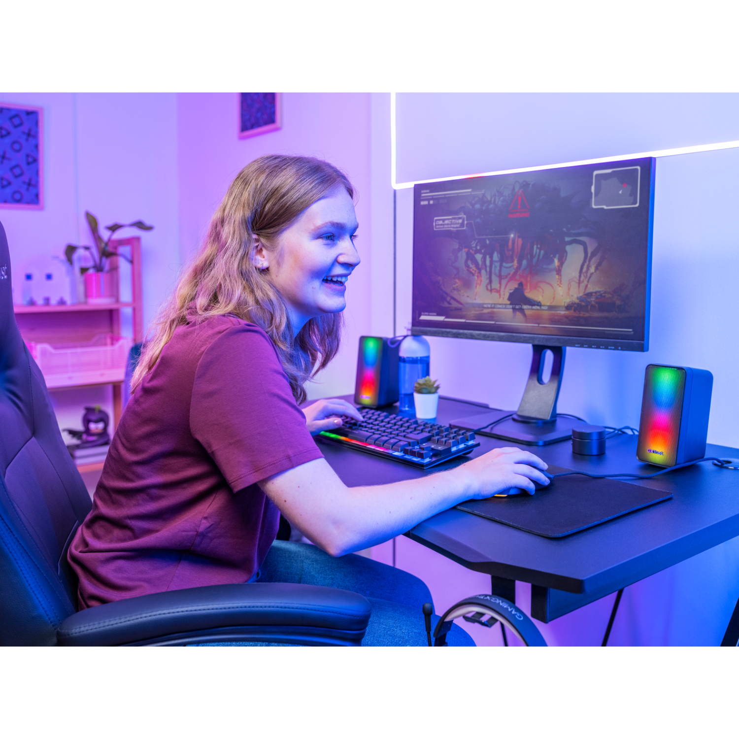 Woman gaming. She is smiling and looking at the screen. Speakers and keyboard are visible.