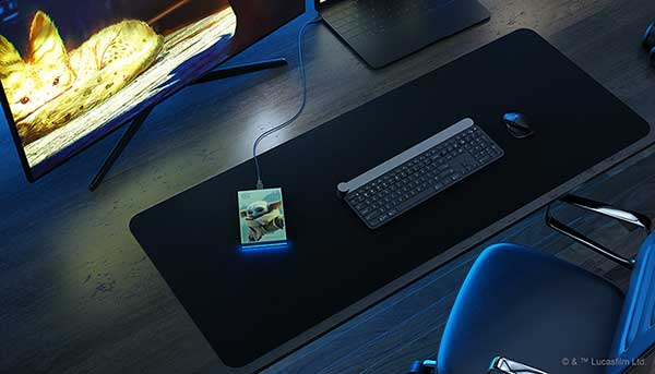 Configuración de escritorio con monitor, teclado, ratón y una base de carga con una imagen de Grogu.