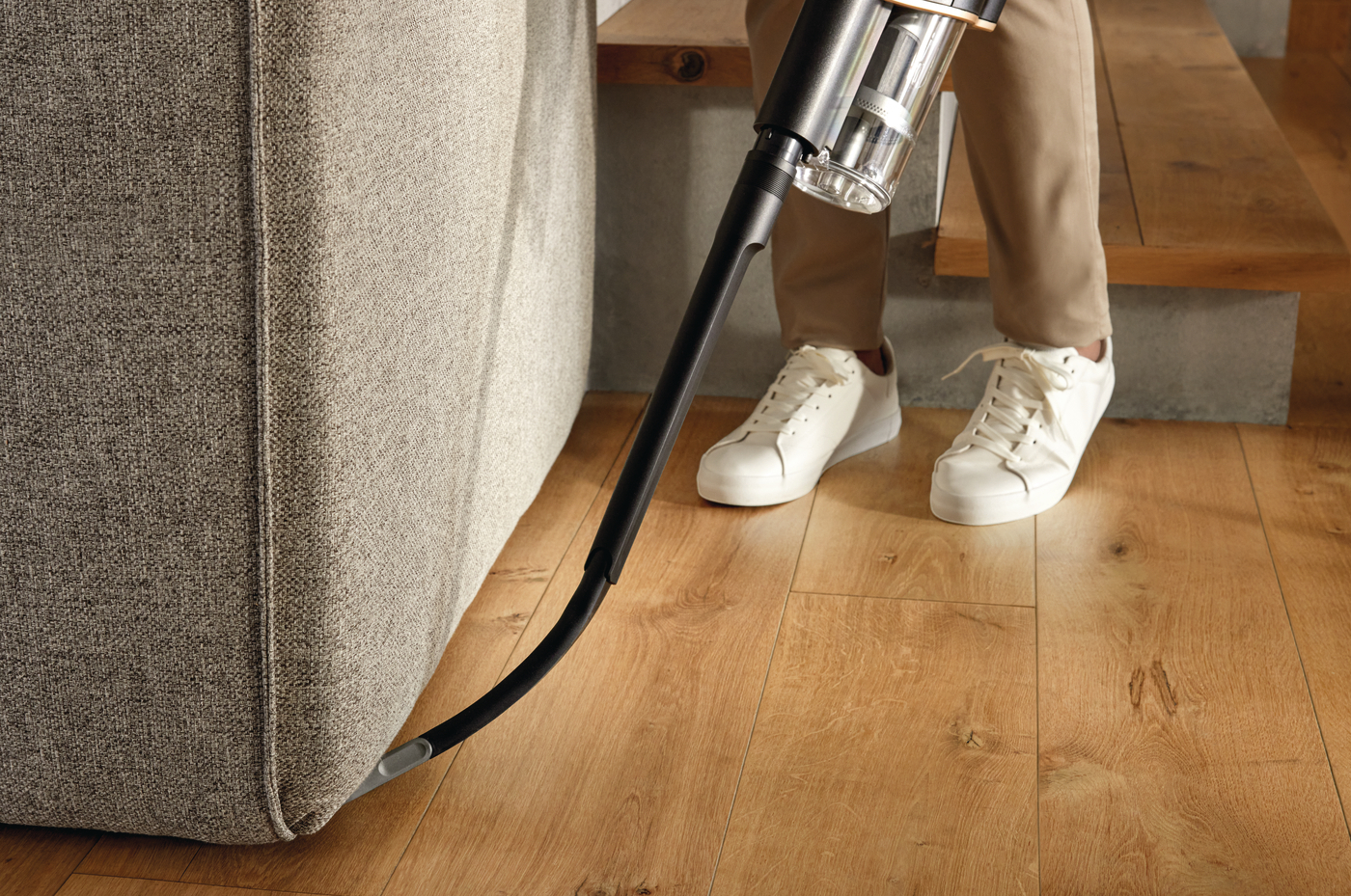 Person saugt einen Holzboden in der Nähe einer Couch mit einem schwarzen Staubsauger.