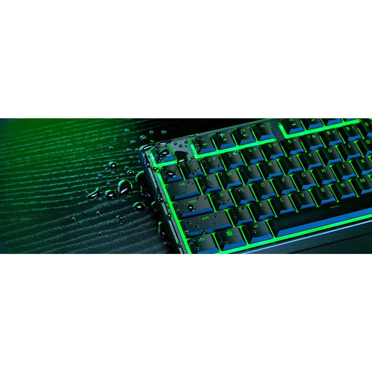 Yeşil arka aydınlatmalı siyah bir oyun klavyesi. Yüzeyde su damlacıkları. Karanlık arka plan.