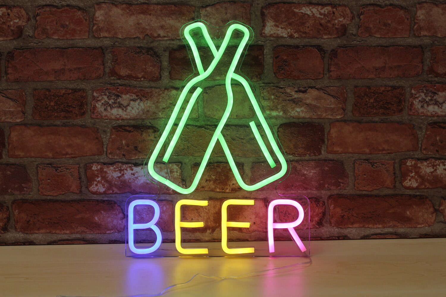 Neonowy znak z napisem BEER w różnych kolorach. Powyżej dwa neonowe butelki piwa.