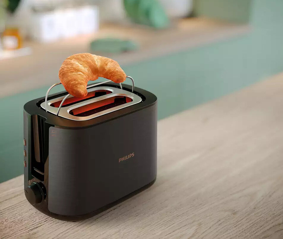 Czarny toster z rogalikiem na wierzchu. Toster stoi na drewnianej powierzchni.