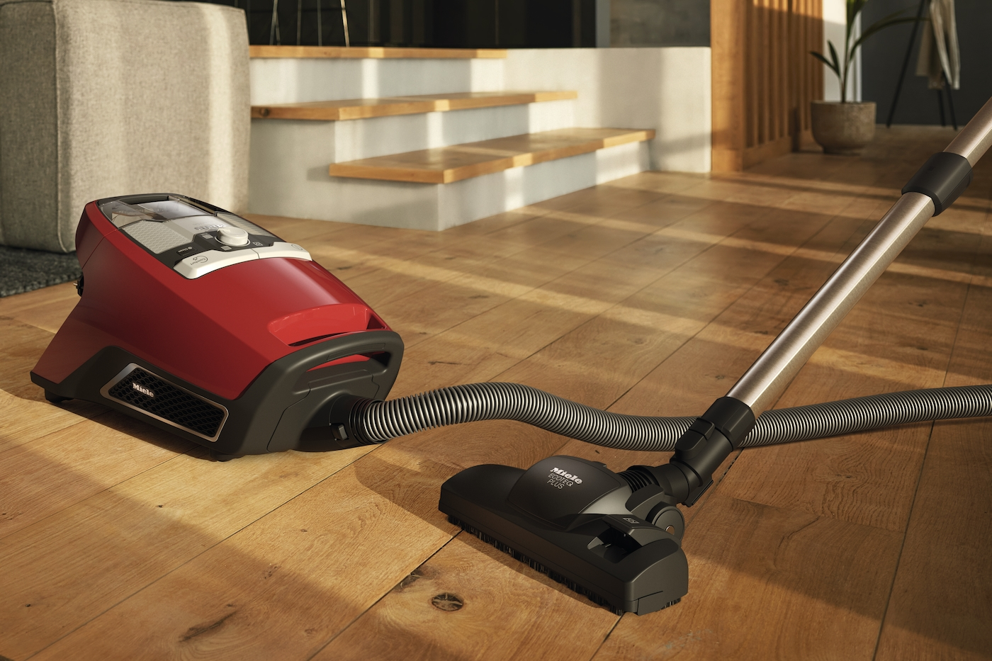Ein roter Miele Staubsauger mit Schlauch und Bürste auf einem Holzboden.