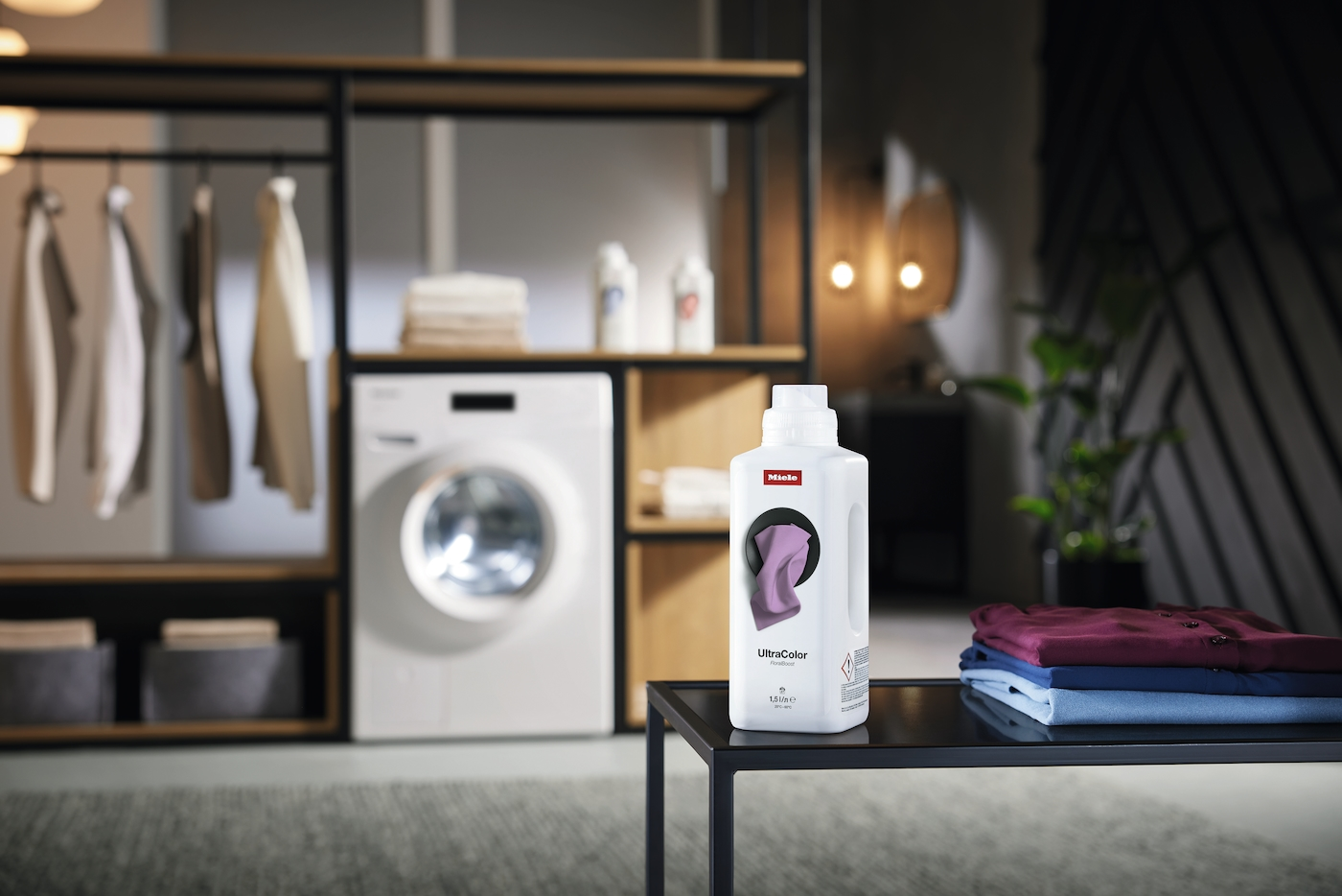 Miele UltraColor Waschmittel neben gestapelter Kleidung und Waschmaschine.