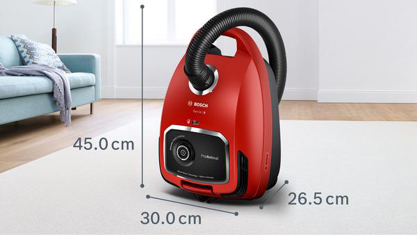 Ein roter Staubsauger mit schwarzen Elementen, der auf einem weißen Teppich steht, mit Maßen.