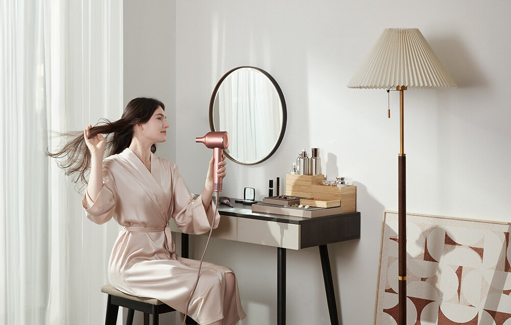 Kobieta używająca suszarki do włosów przed lustrem i toaletką.