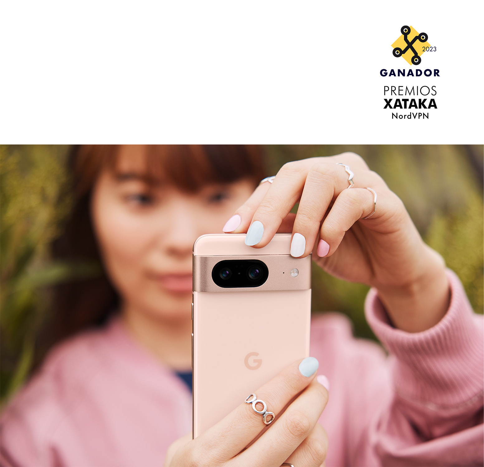 Mujer sosteniendo un teléfono rosa, con uñas rosas y azules. El fondo está borroso.