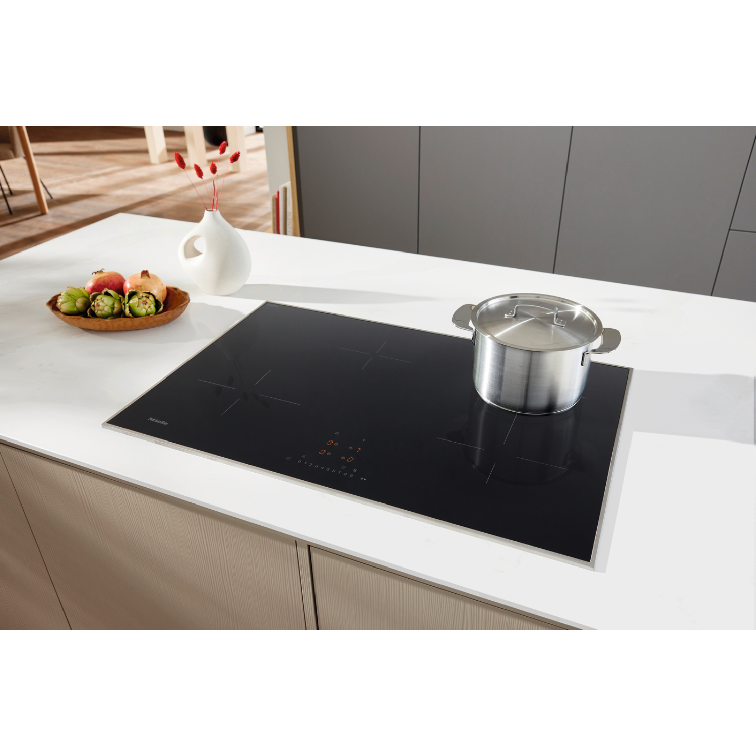 A pot on an induction hob with a fruit bowl and vase nearby.