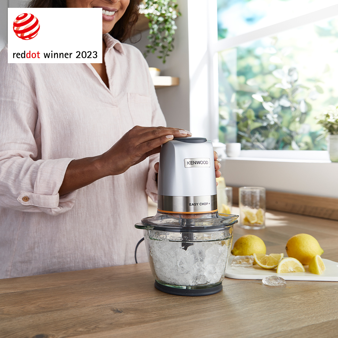 Donna usa tritatutto Kenwood con ghiaccio e limoni su un bancone di legno vicino a una finestra.