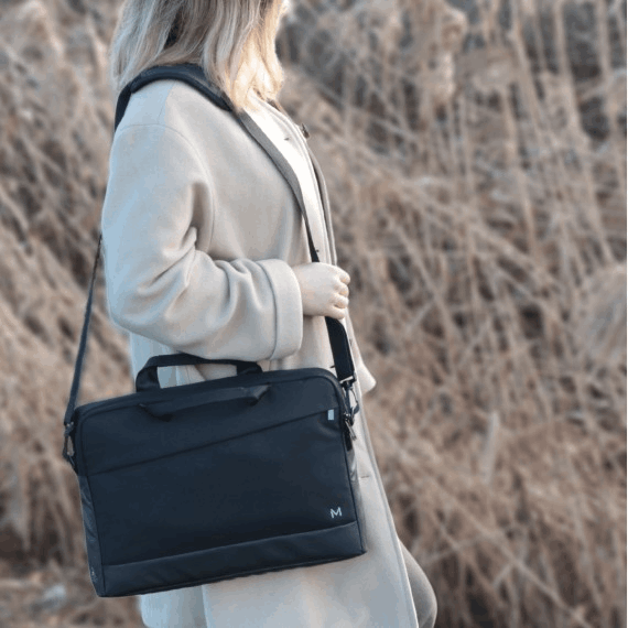 Mujer llevando una bolsa negra para portátil, caminando por hierba alta y seca.
