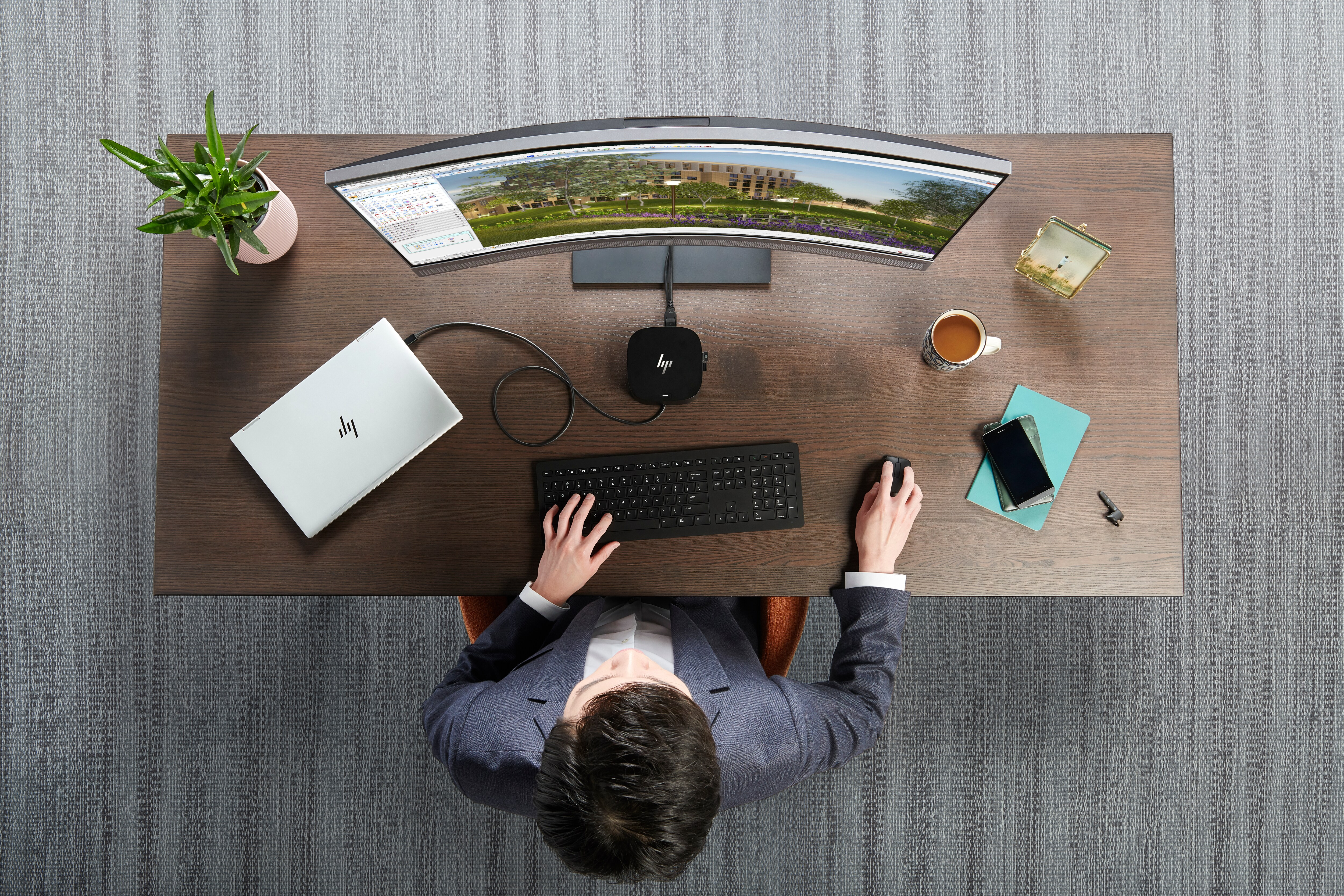Bürotisch mit Laptop, Tastatur, Dockingstation und eine Person arbeitet.