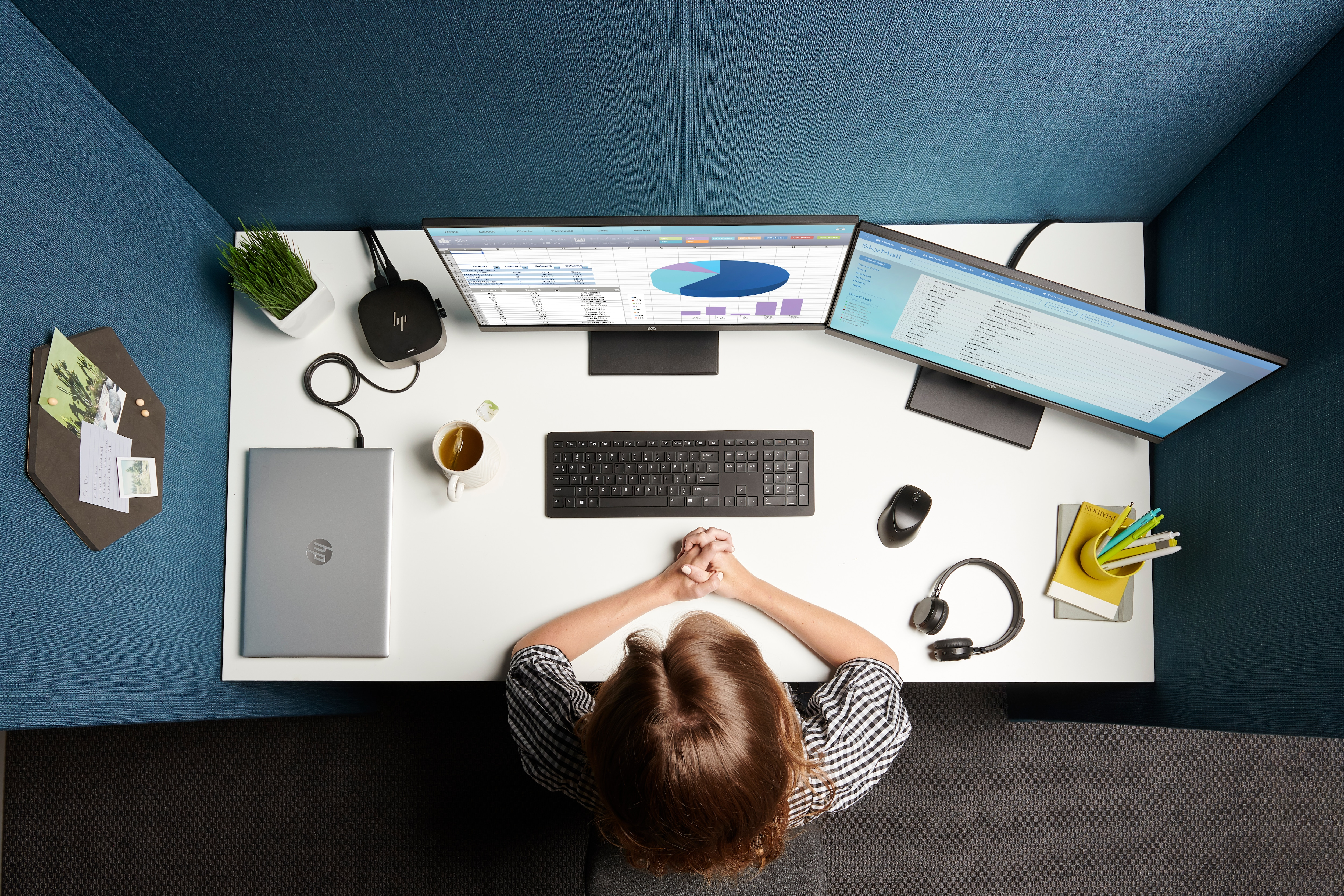 Ein Büroszene mit zwei Monitoren, einem Laptop und eine Person arbeitet.