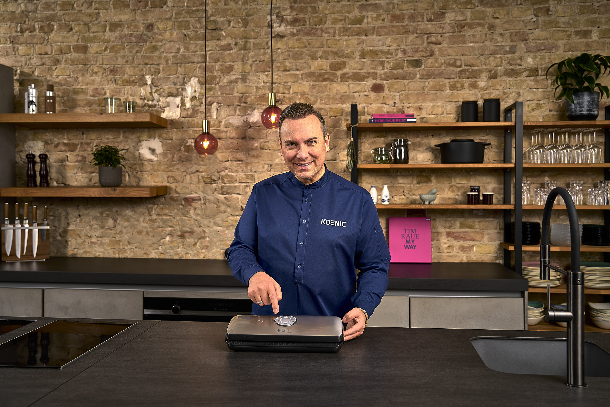 Ein Mann in blauem Hemd bedient ein Küchengerät. Ziegelwandhintergrund.