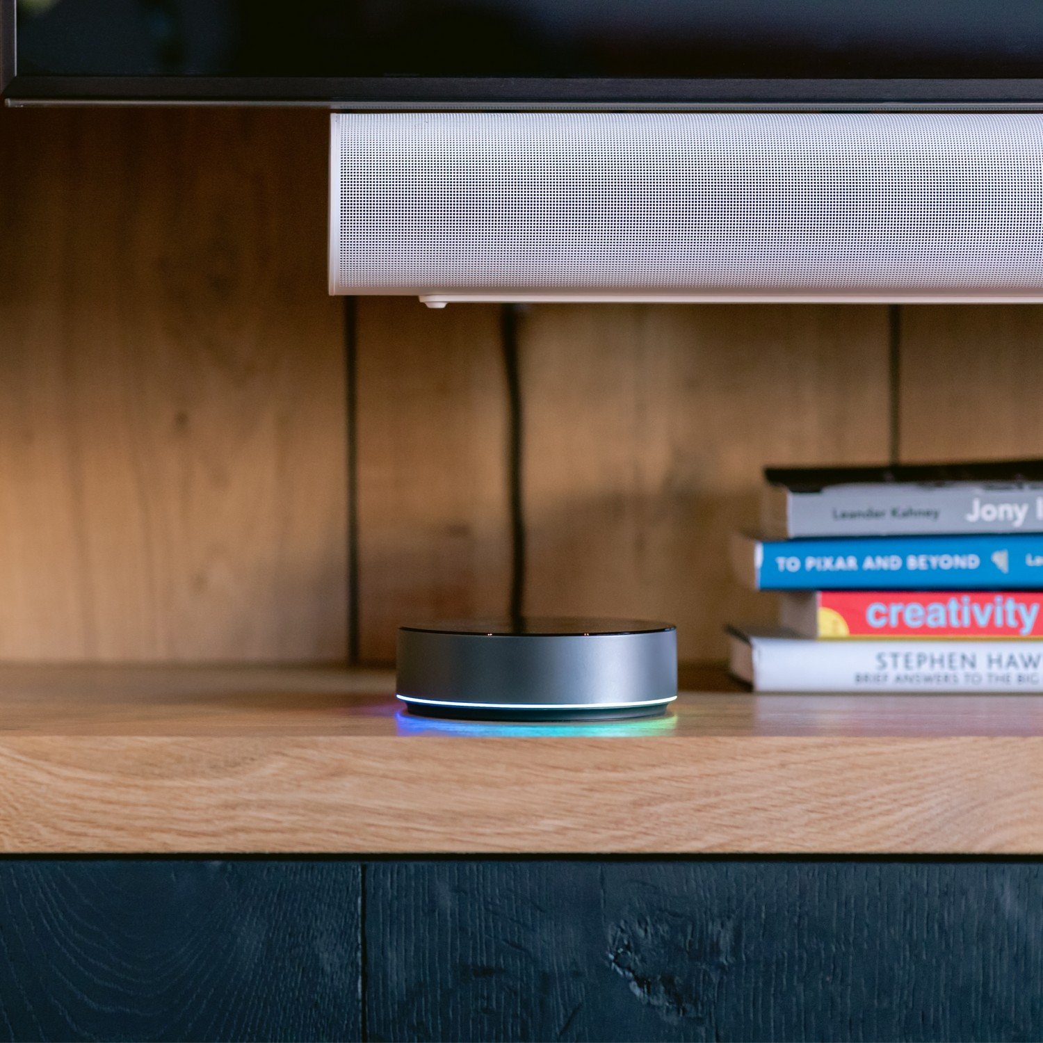 Smart home hub on a wooden surface, with books and a soundbar in the background.