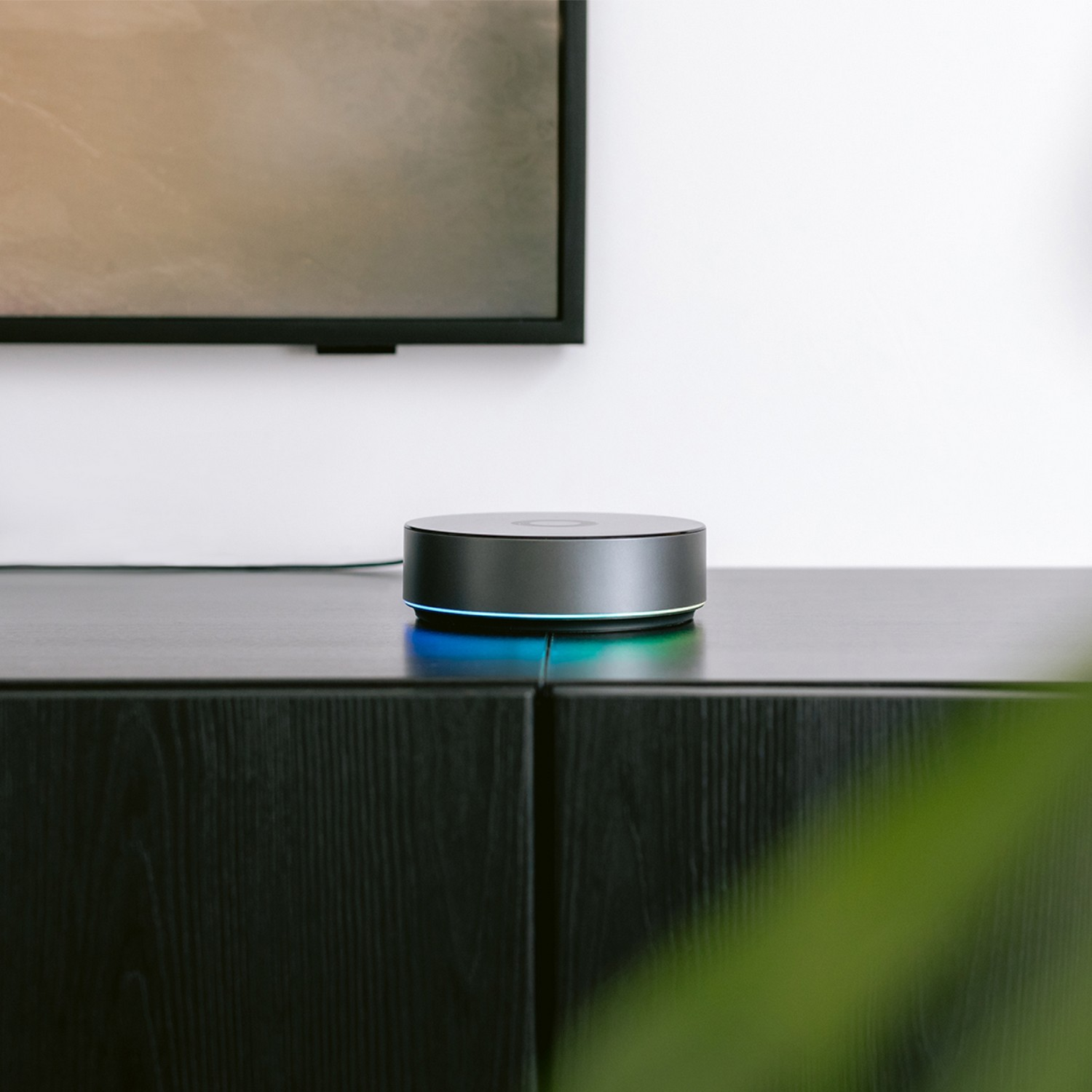Smart home hub on a black cabinet with a television in the background.