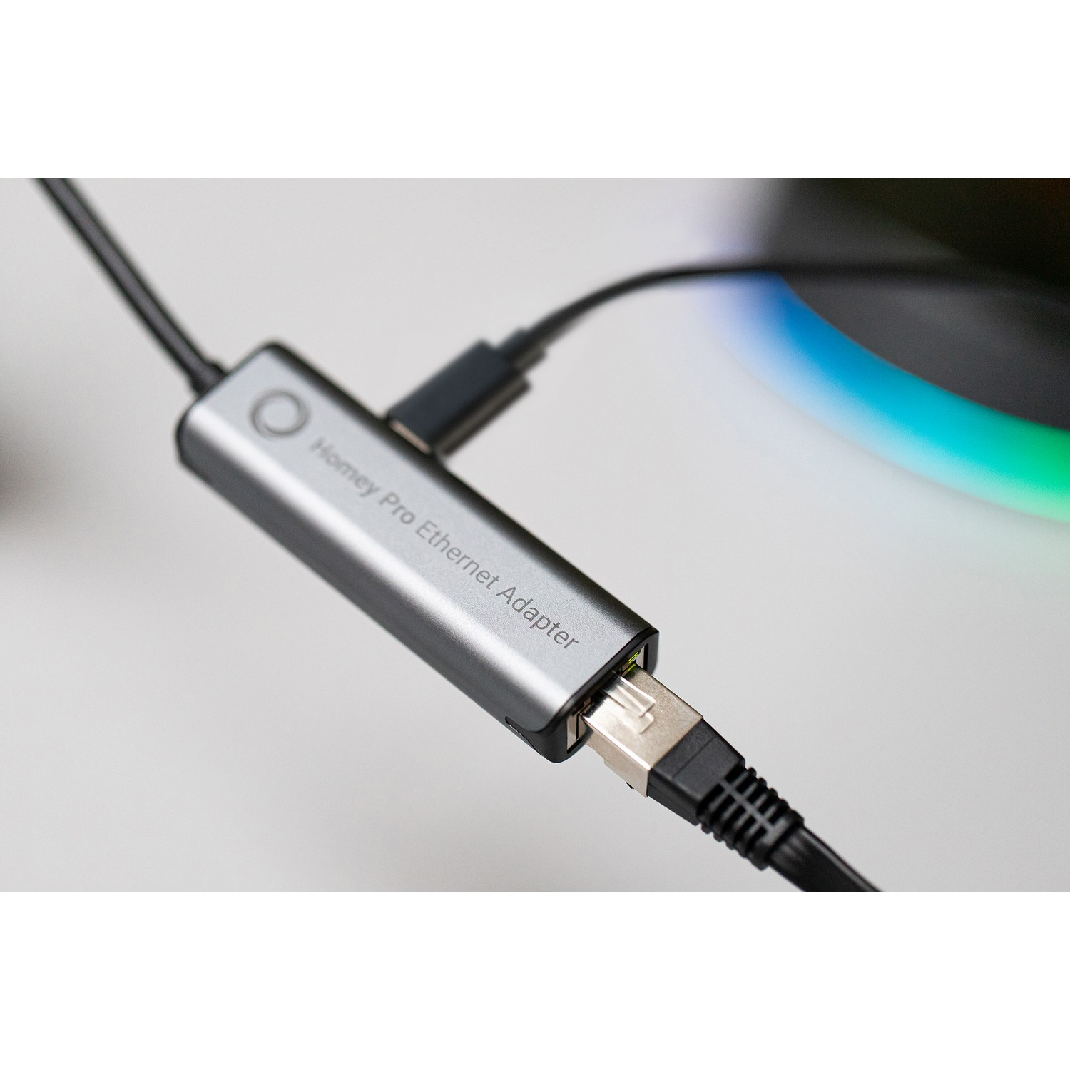 A silver Homey Pro Ethernet Adapter with cables connected, close-up on a white surface.