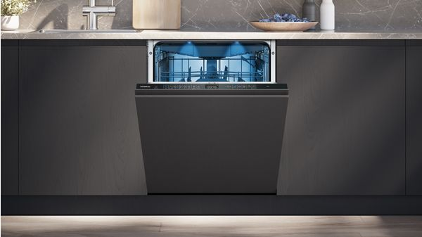 Un lavavajillas empotrado con puerta abierta, interior iluminado, cocina oscura.