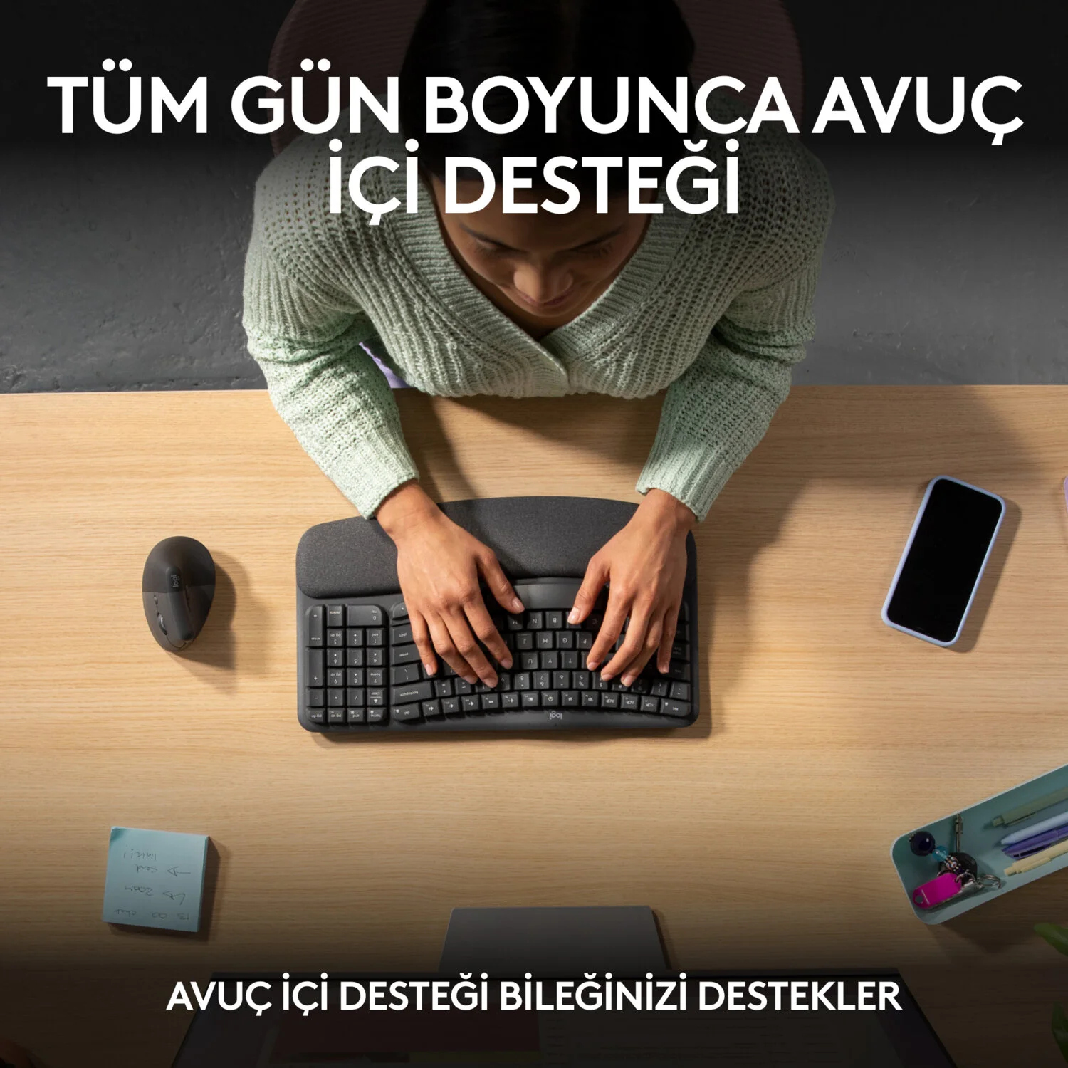 Bileklik dayanağı olan bir klavyede yazan bir kişi, bir farenin ve bir akıllı telefonun yanında.