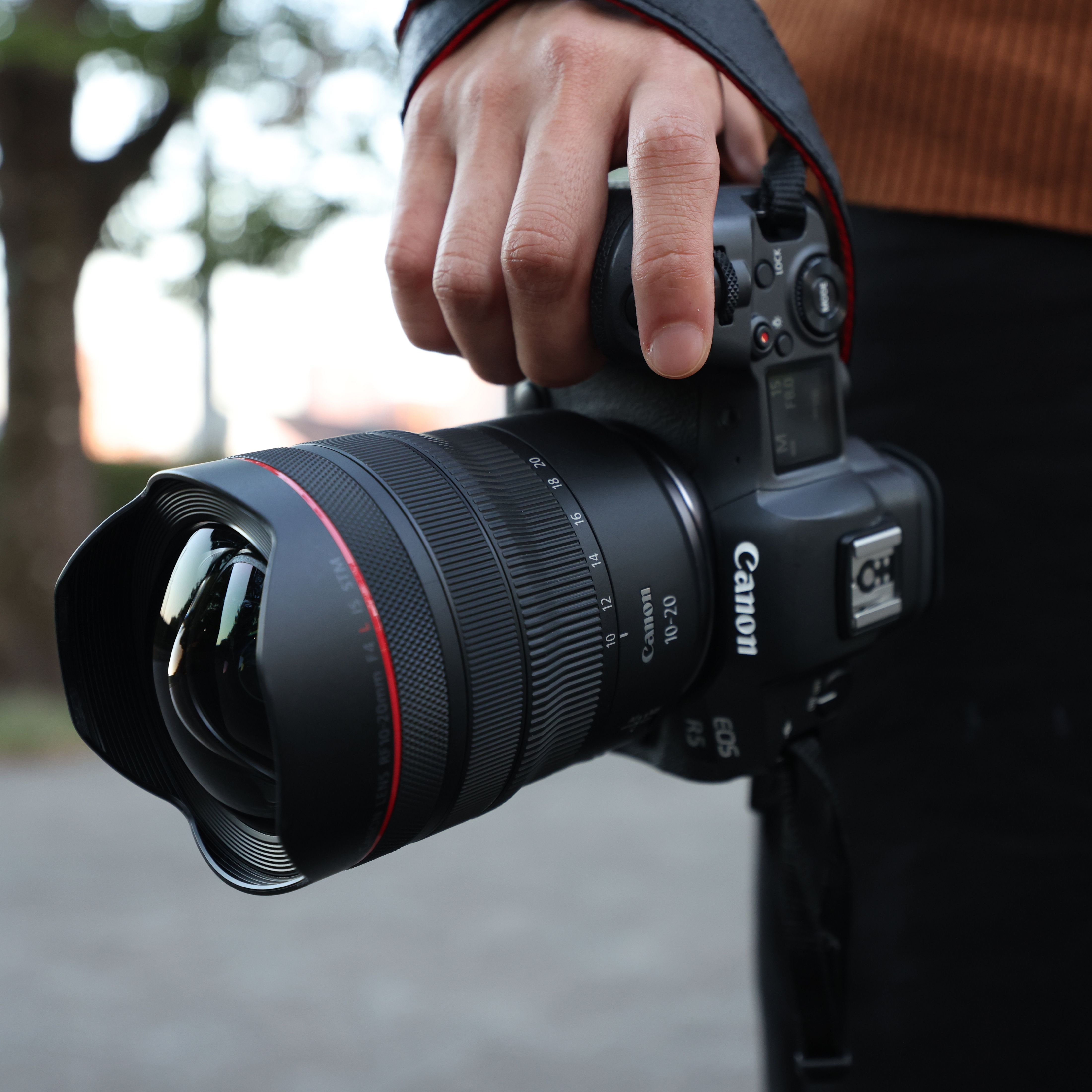 Une main tient un appareil photo Canon EOS R5 avec un objectif 10-20mm.