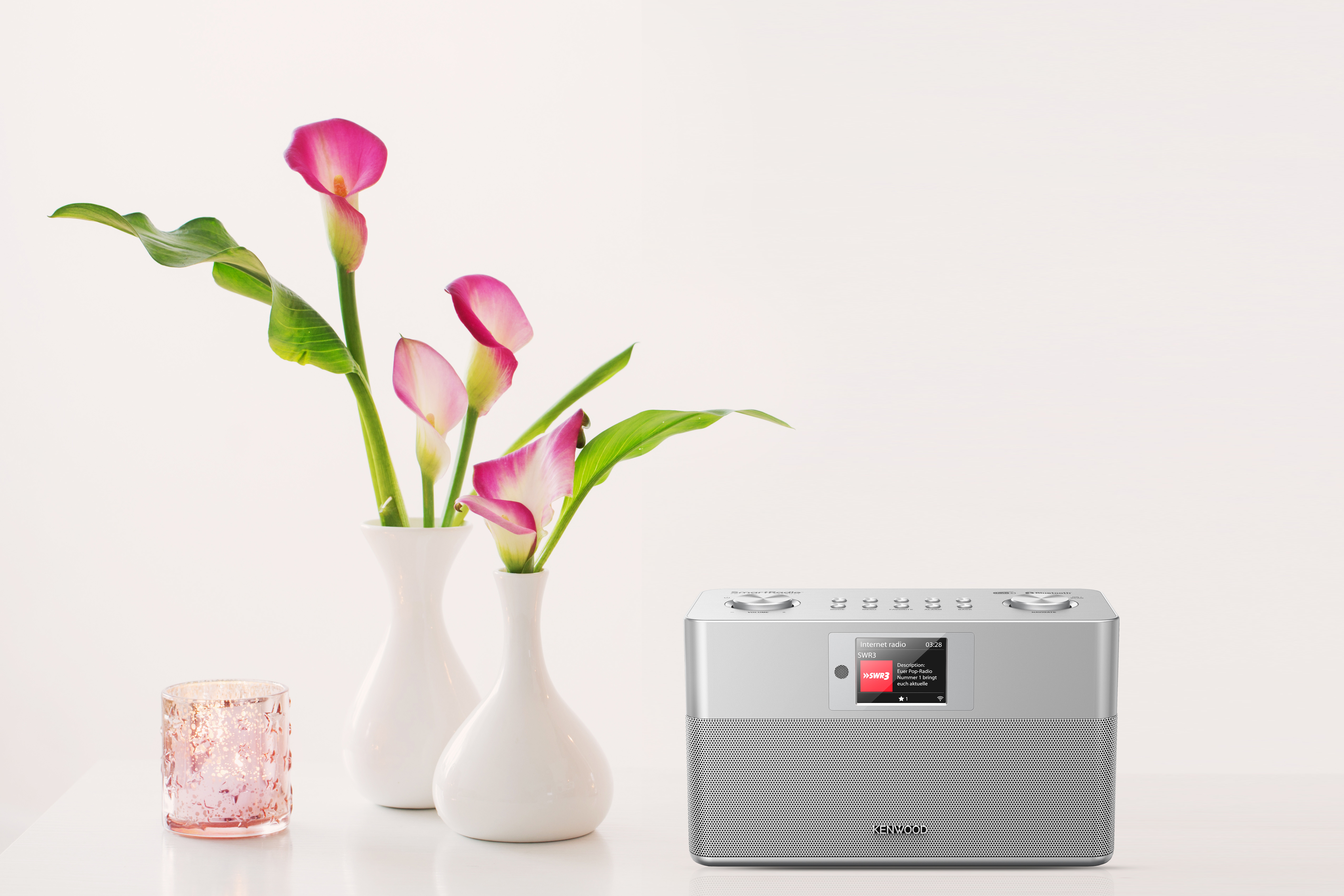 Modernes silbernes Internetradio mit Blumen in weißen Vasen und einer Kerze.