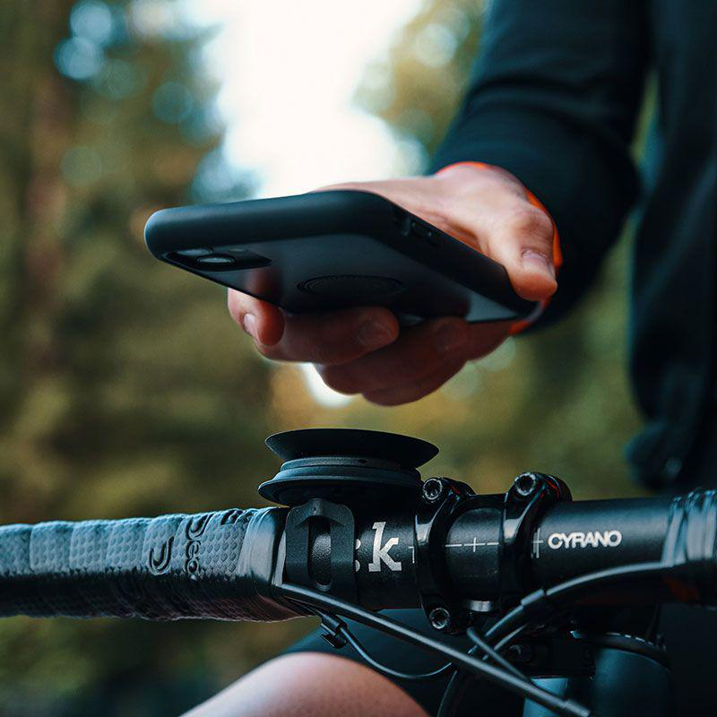 Eine Person, die ein Telefon hält, das an einem Fahrradlenker befestigt ist, schwarzes Telefon und Halter, grüner Hintergrund.