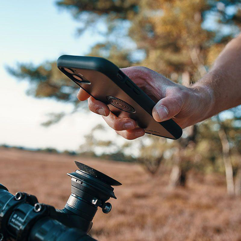 Die Hand einer Person hält ein Telefon in einer schwarzen Hülle, mit einer Halterung am Fahrradlenker.