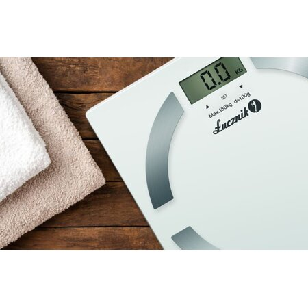 Biała cyfrowa waga łazienkowa z wyświetlaczem pokazującym 0,0 kg, na drewnianej powierzchni.