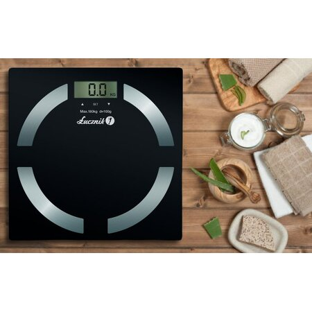 Czarna cyfrowa waga łazienkowa na drewnianej powierzchni z aloesem, kremem i ręcznikami.