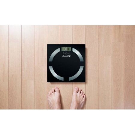 Czarna cyfrowa waga łazienkowa na drewnianej podłodze, z dwoma nagimi stopami na niej.