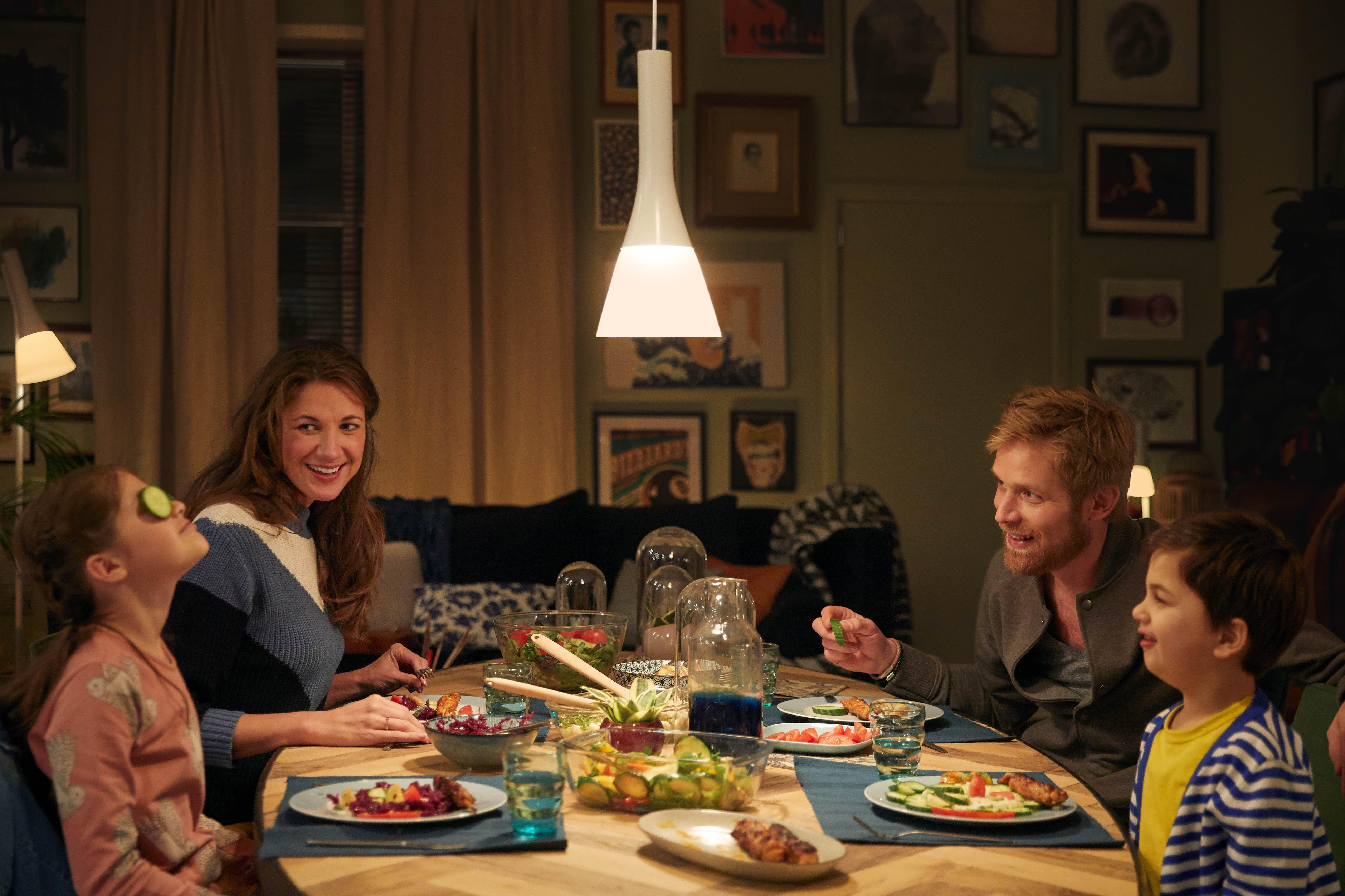 Familie am Esstisch mit Essen. Über dem Tisch hängt eine Lampe.