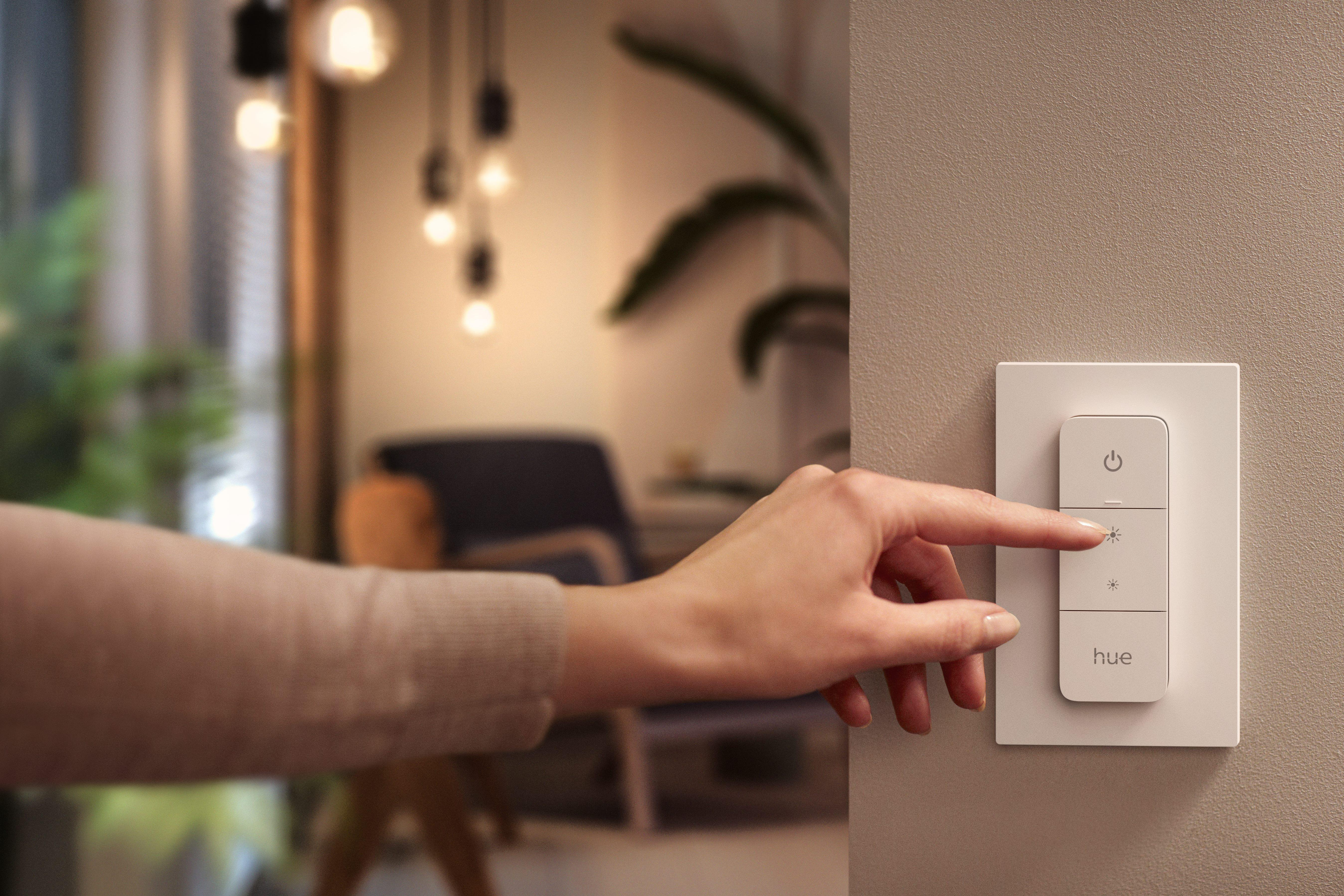 Eine Hand drückt eine Taste auf einem weißen, an der Wand montierten intelligenten Lichtschalter.