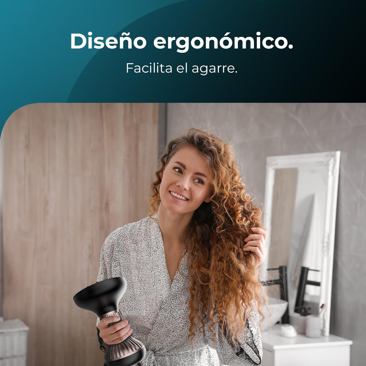 Mujer secando su cabello con un difusor negro. Espejo y baño en el fondo. Sonriendo y mirando a la cámara.
