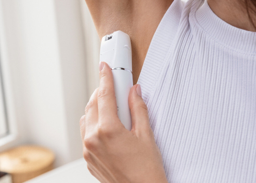 Kobieta używająca białego depilatora pod pachą. Białe tło.