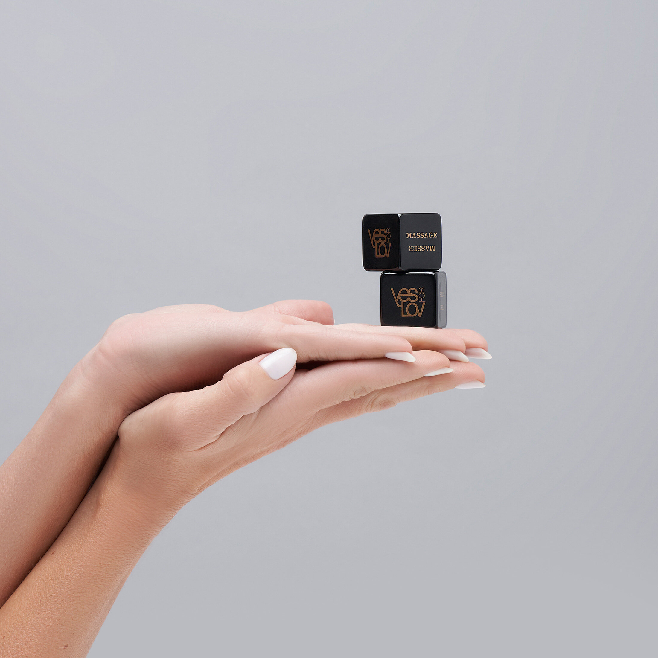 Dłonie trzymające dwie czarne kostki do masażu ze złotym tekstem na białym tle.