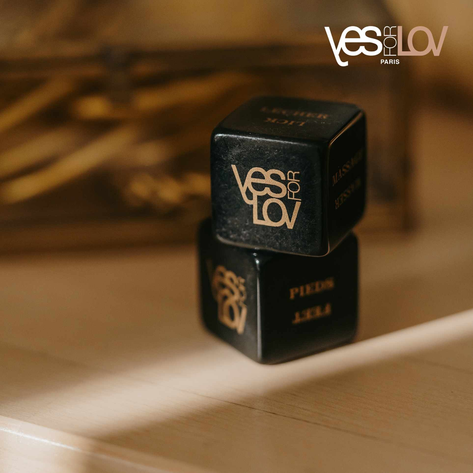 Dwie czarne kostki ze złotym tekstem 'yes for lov' ułożone na drewnianej powierzchni.