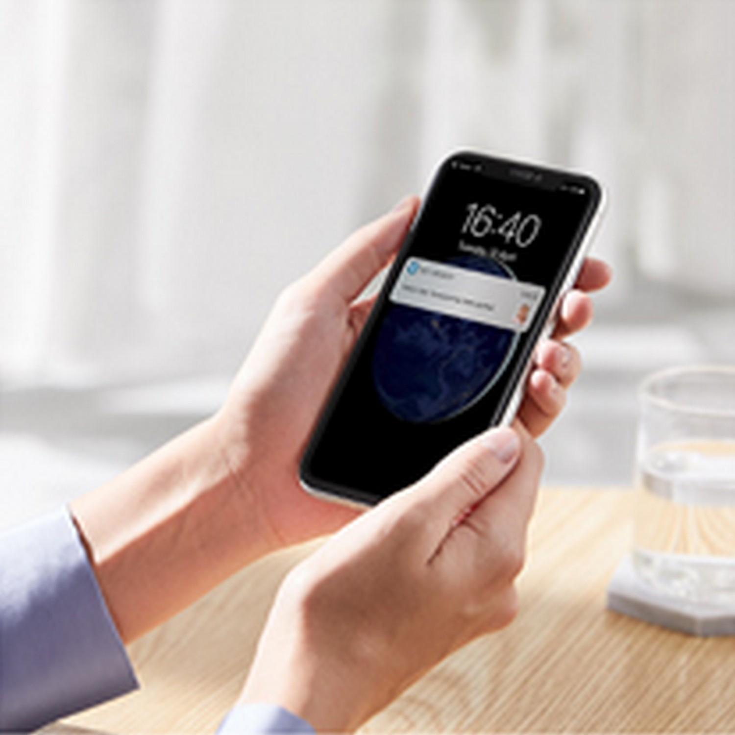 Mains tenant un smartphone affichant une notification. Un verre d'eau est sur la table.