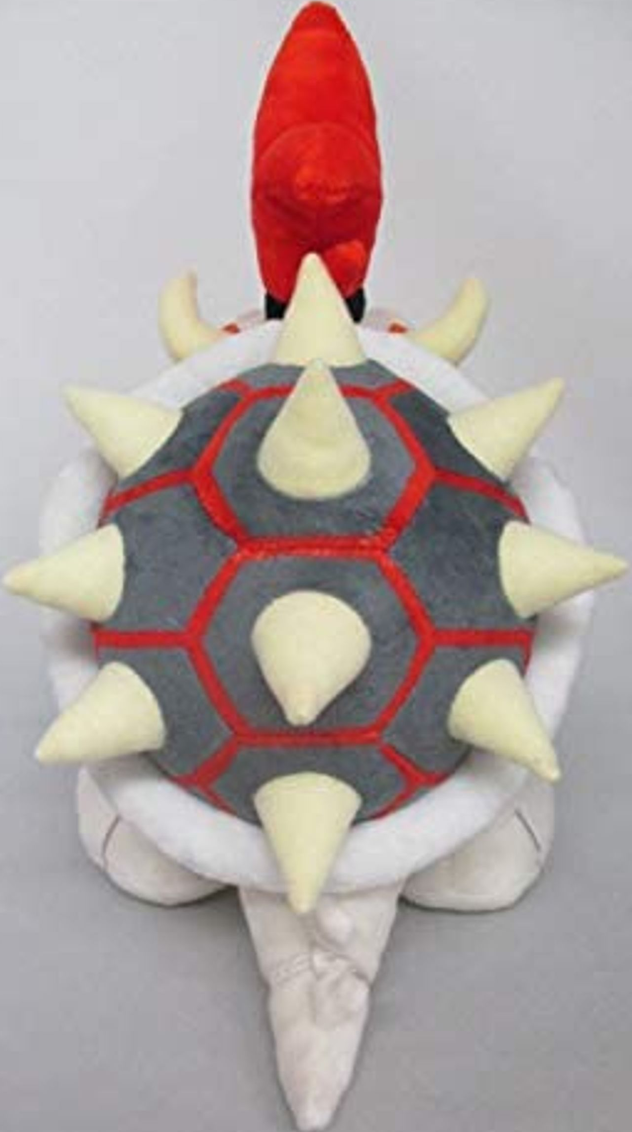 Une peluche Koopa Troopa, carapace grise avec détails rouges, corps blanc, tête rouge.