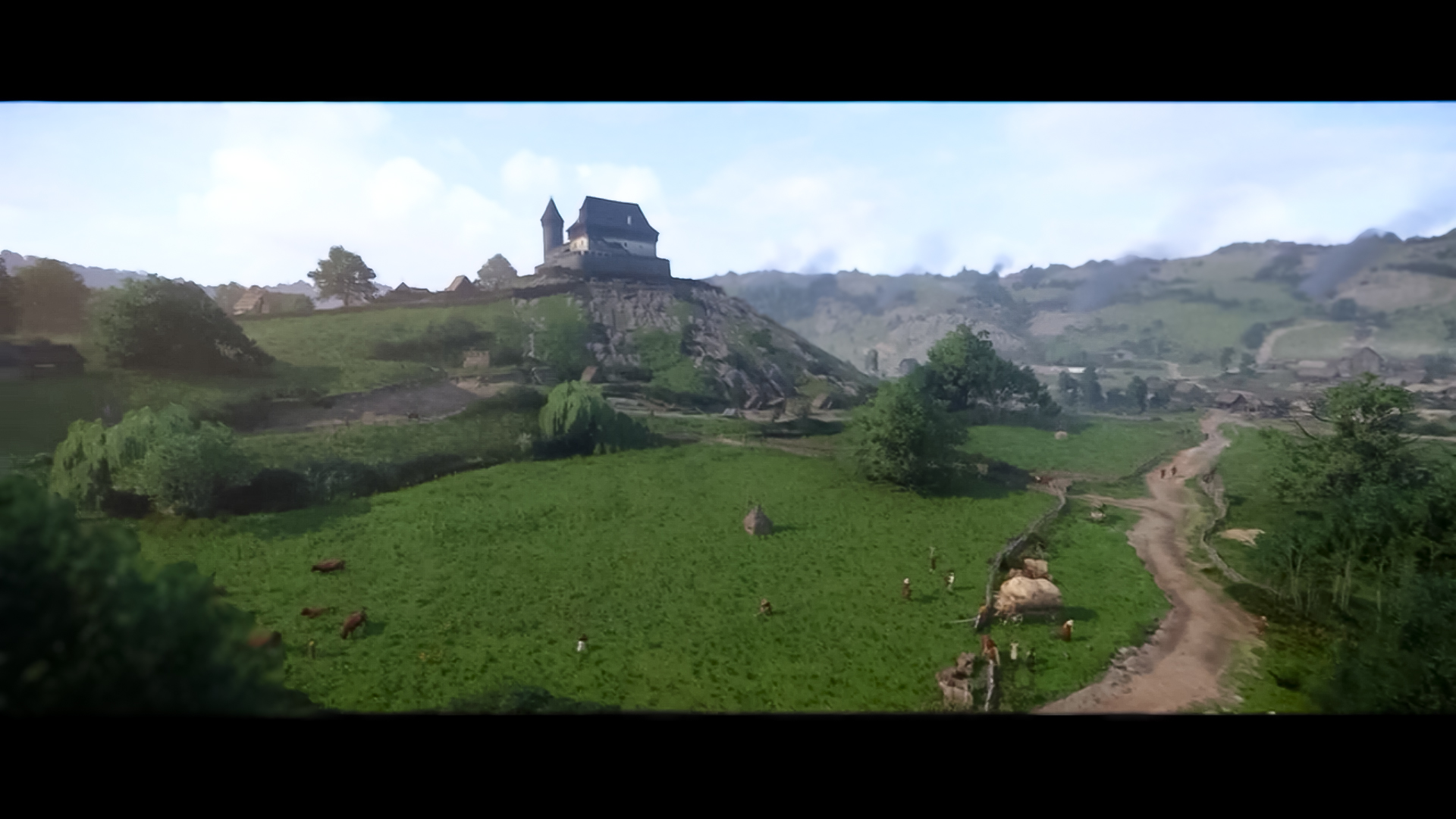 Landschaft mit Burg auf einem Hügel, grünen Feldern, Kühen und einem Dorf. Der Himmel ist bedeckt.