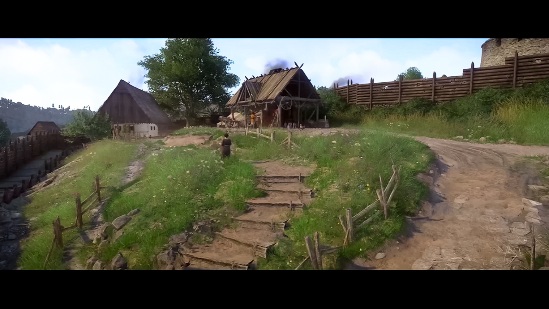 Dorfansicht mit Holzzäunen, Häusern und einer Steintreppe bergauf.