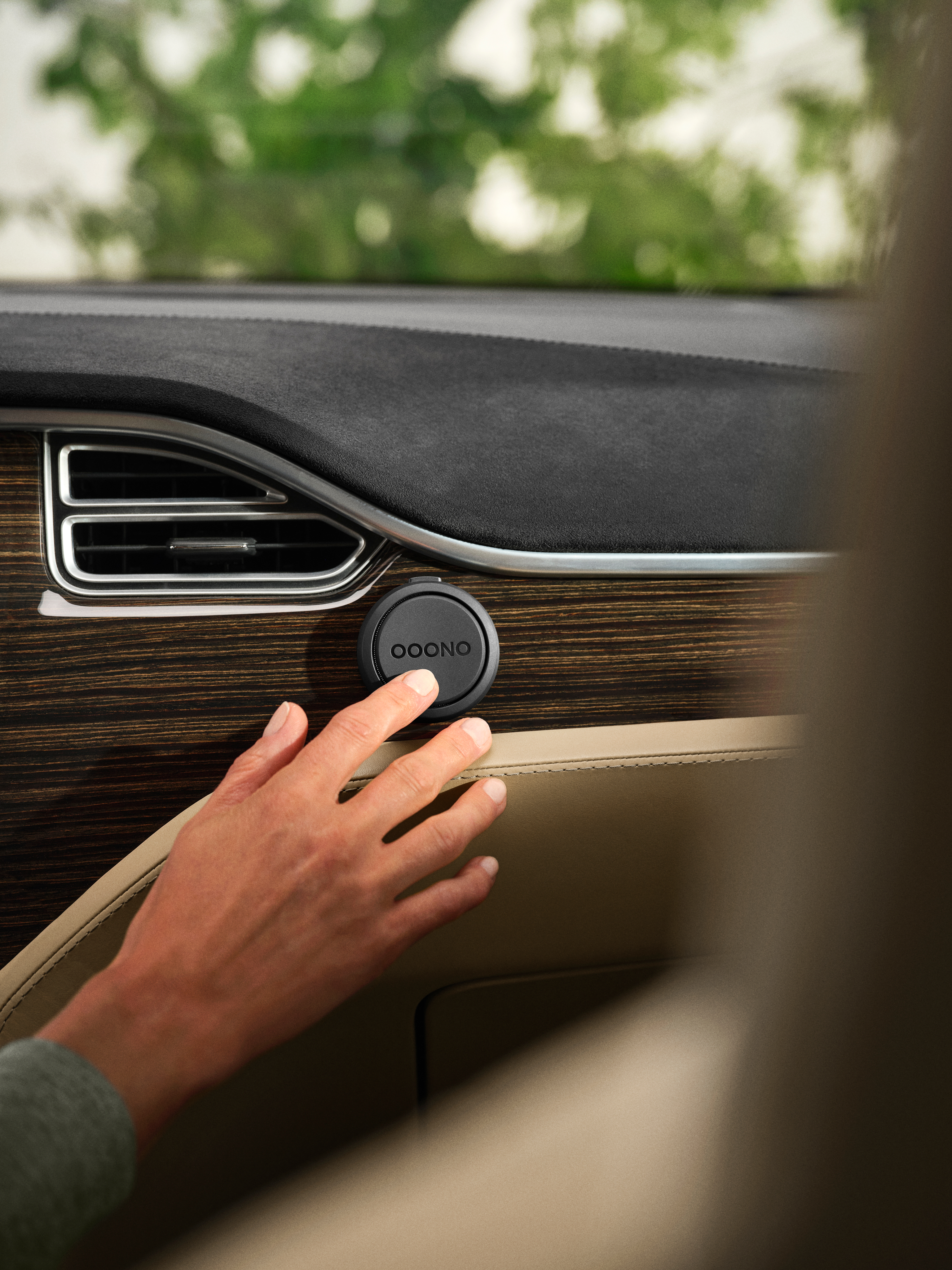 Ein schwarzes Ooono-Gerät auf dem Armaturenbrett eines Autos wird von einer Hand berührt.