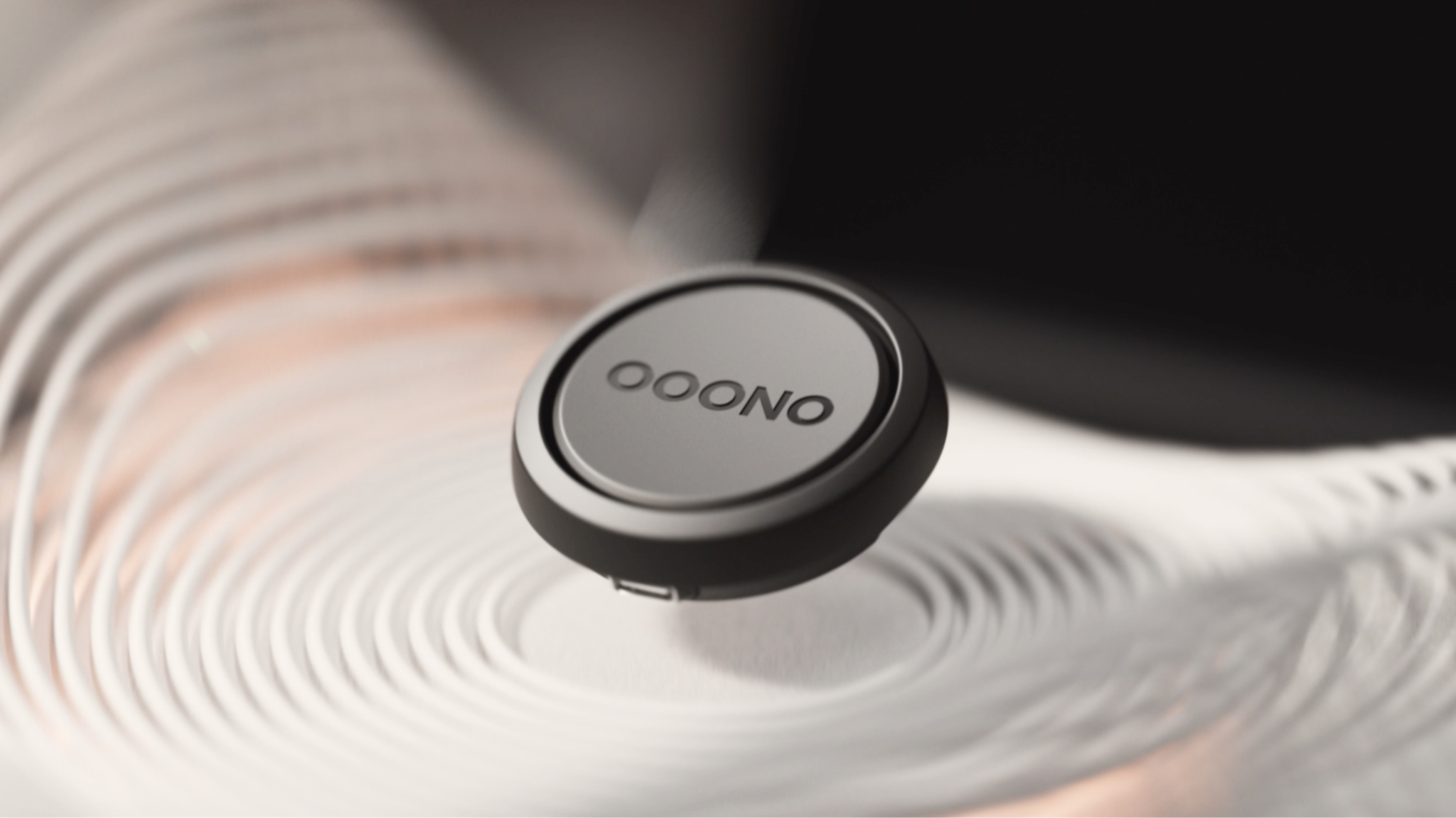 Ein kleines, rundes, graues Gerät mit dem Wort "OOONO" darauf, vor verschwommenem Hintergrund.