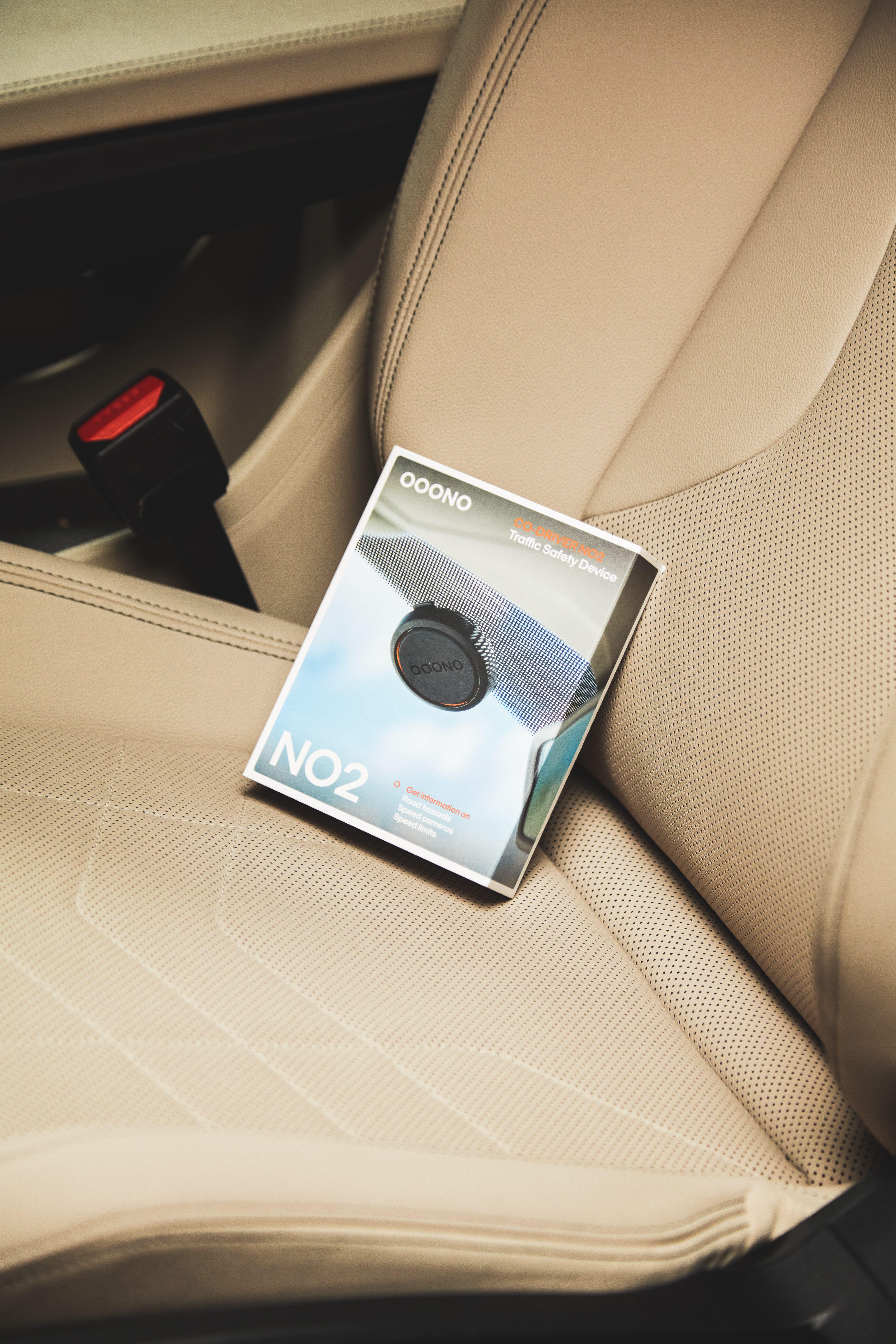 Box mit der Aufschrift 'Ooono' mit einem Autospiegelgerät, in einem beigen Autositz. Sicherheitsgurt sichtbar.