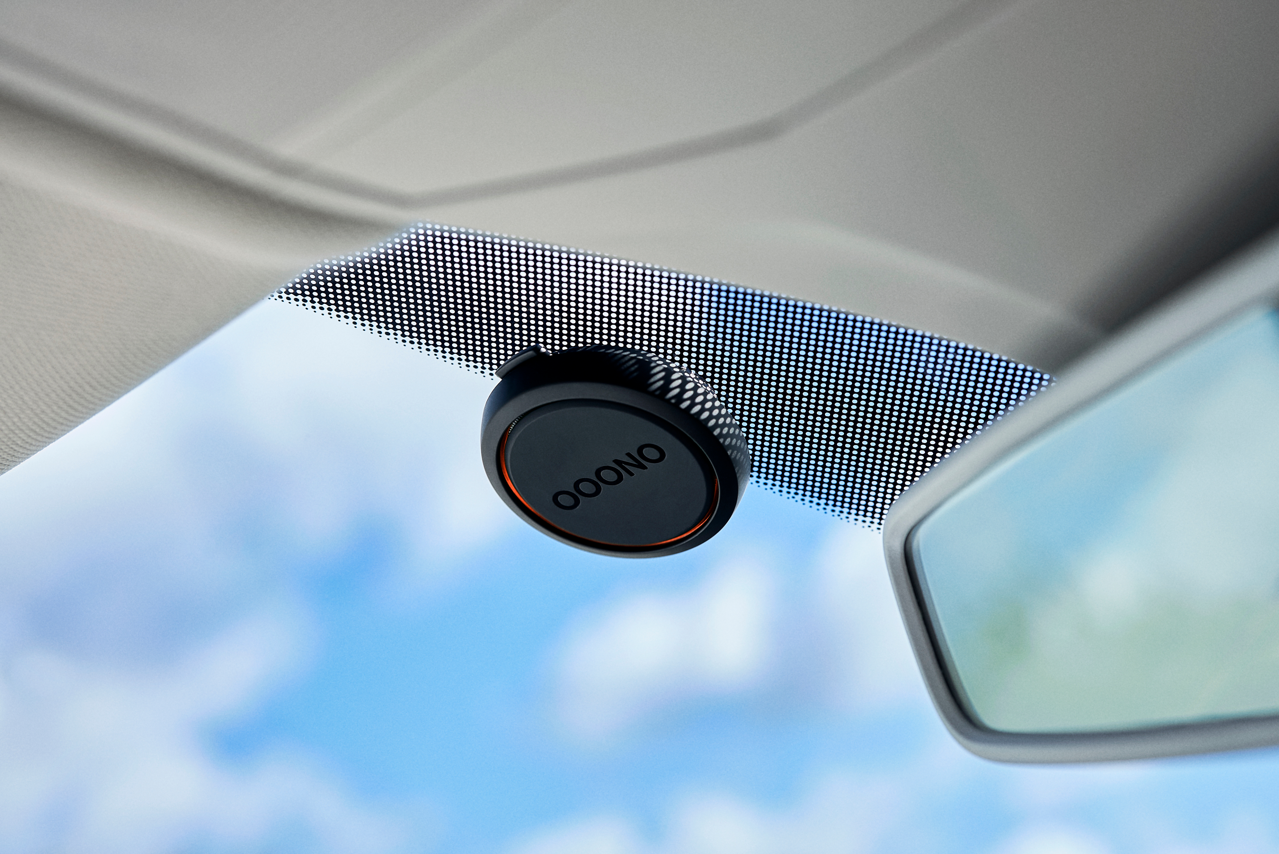Der Innenraum eines Autos zeigt ein schwarzes Gerät an der Windschutzscheibe, mit blauem Himmel im Hintergrund.