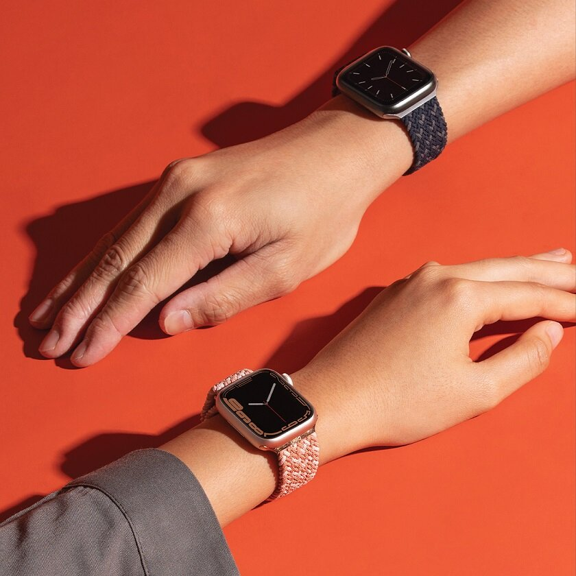 Dwa nadgarstki noszące smartwatche z różnokolorowymi paskami na pomarańczowym tle.