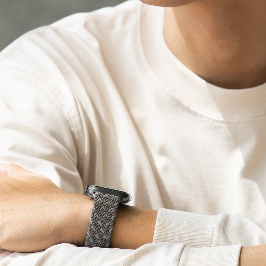 Nadgarstek osoby z szaro-białym plecionym paskiem do zegarka i białą koszulą.