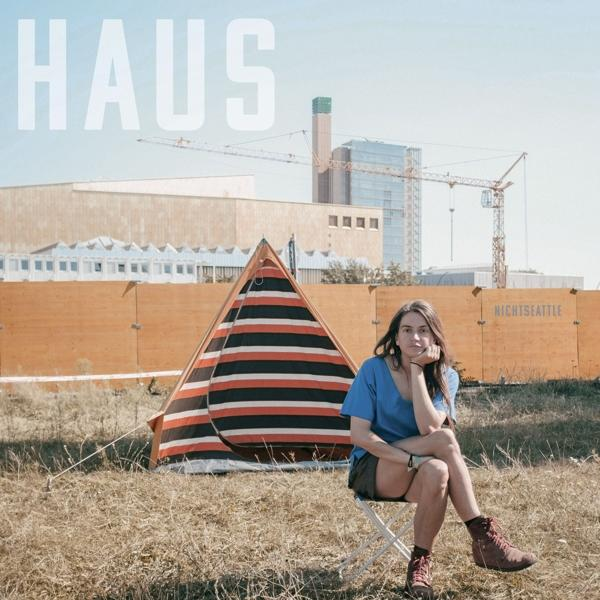 Eine Frau sitzt in der Nähe eines gestreiften Zeltes. Gebäude und ein Kran im Hintergrund.
