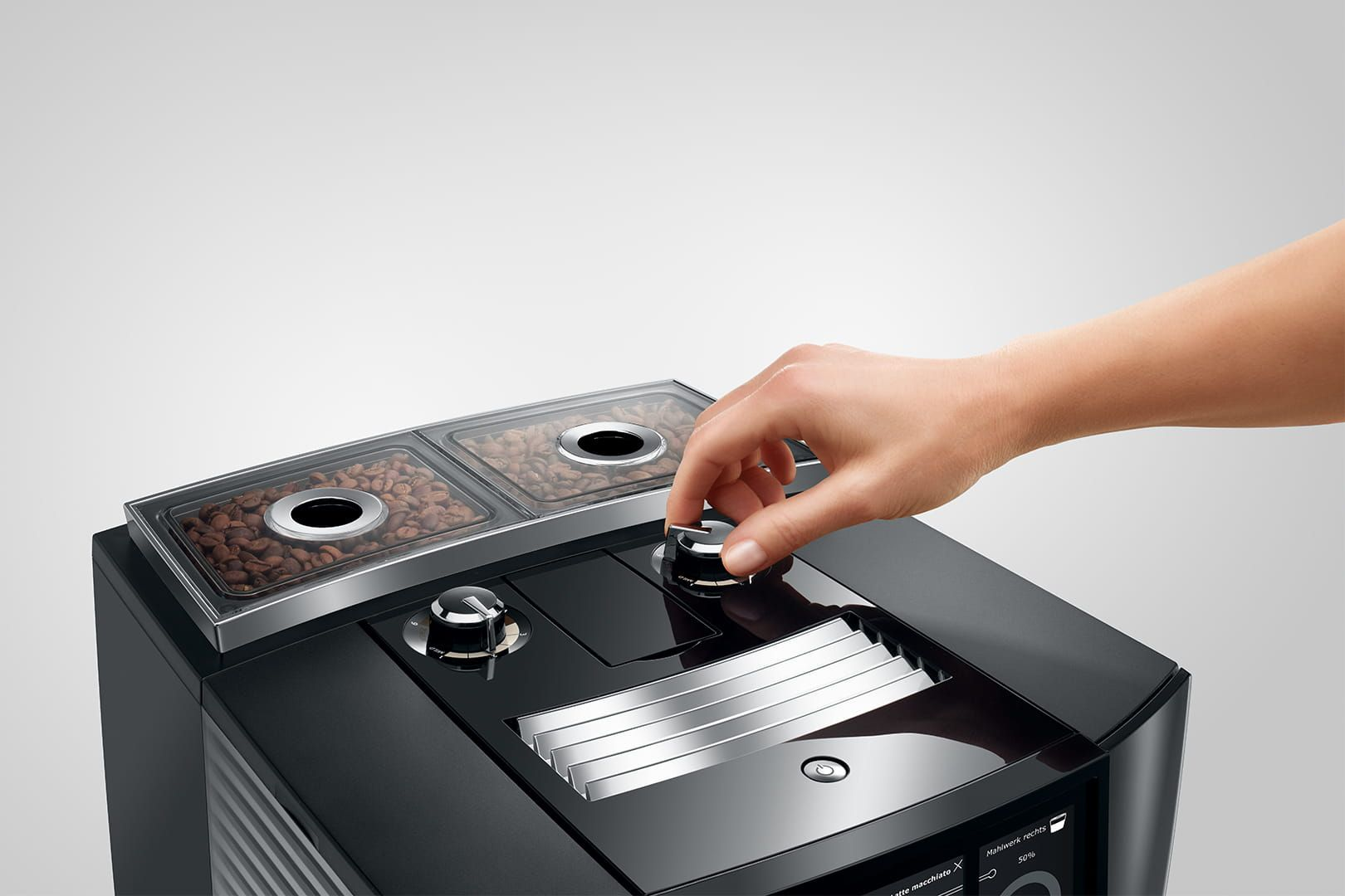 Nahaufnahme einer schwarzen Kaffeemaschine, eine Hand dreht einen Drehknopf über Bohnen.