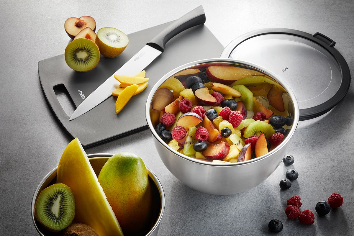 Eine Schüssel mit Obstsalat mit Messer und Schneidebrett. Beeren, Kiwi und Pfirsiche.
