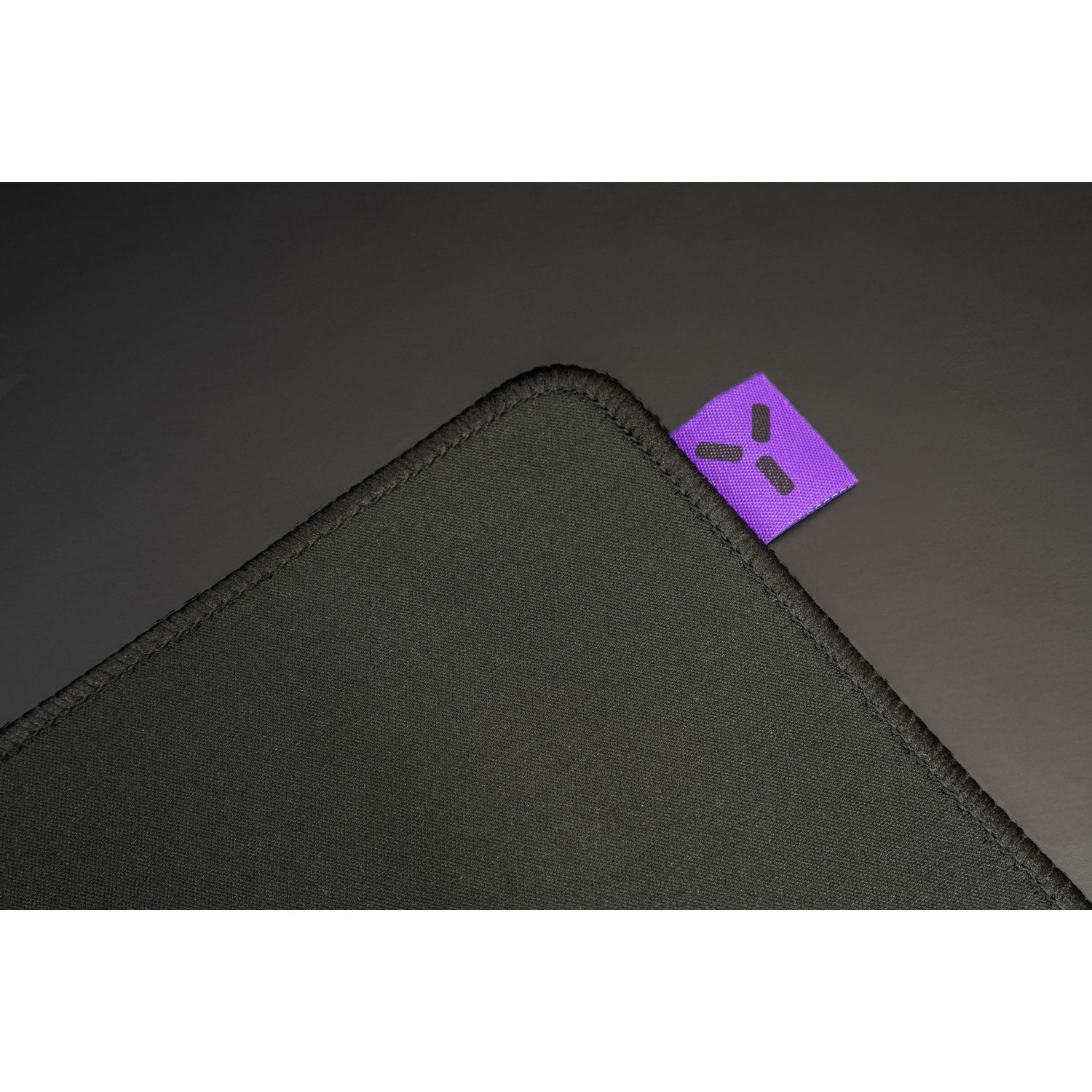 Close-up of a black mousepad with a small purple tag featuring a black logo.