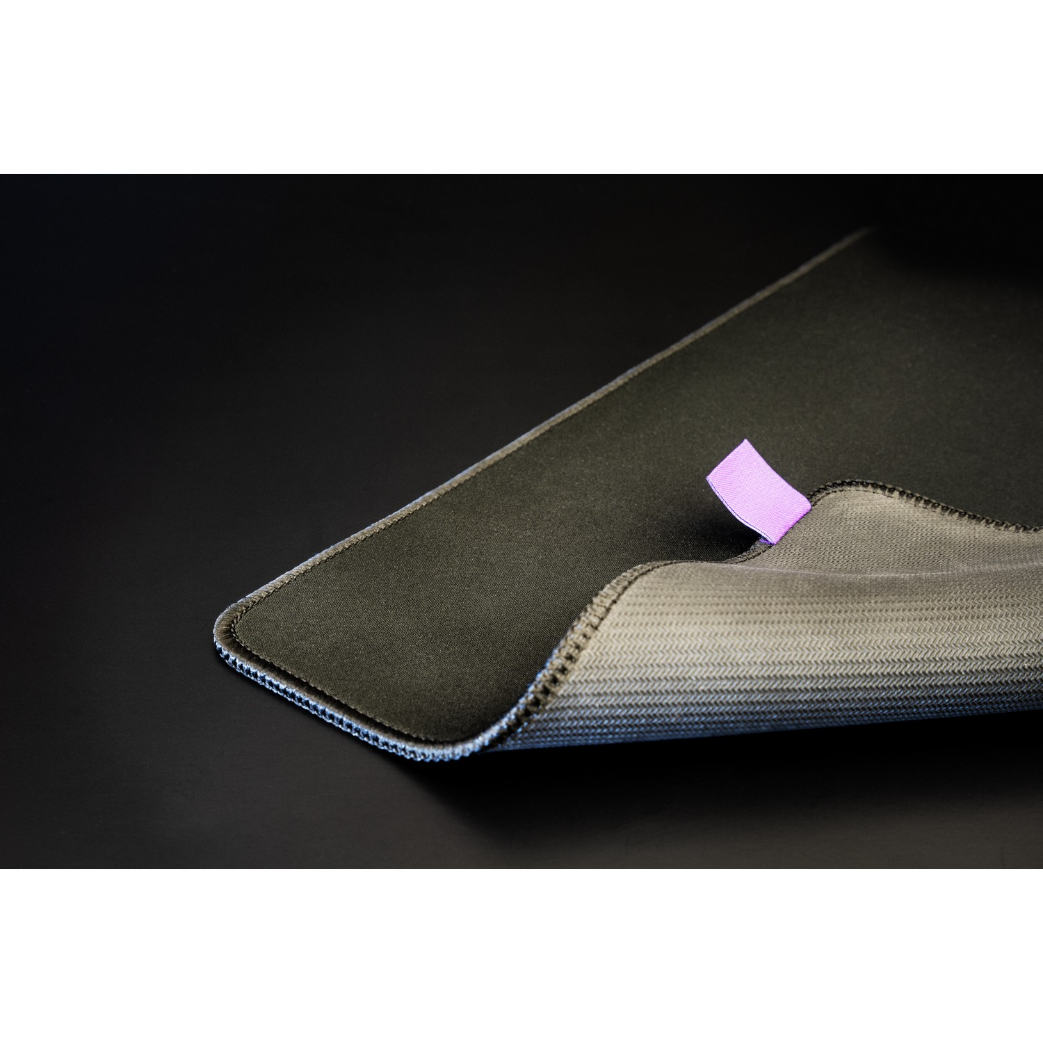 Black mousepad with a small purple tag, resting on a dark surface.